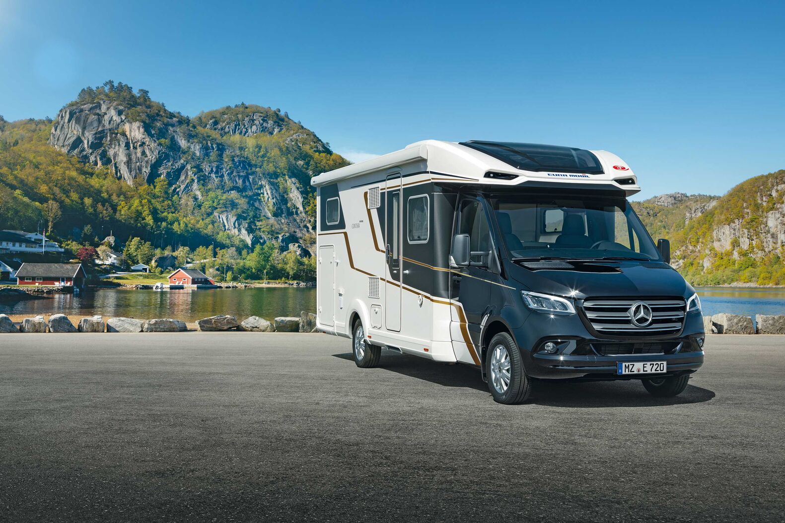 Eura Mobil Contura auf Mercedes-Benz: Bereits im Aussendesign macht der Contura auf dem Mercedes-Benz seinen exklusiven Anspruch deutlich. Das manifestiert sich insbesondere in der Gestaltung mit markanten Lichtkanten und flacher Anbindung zwischen Fahrerhaus und modernem GFK-Aufbau. Das moderne RIM-Fertigungsverfahren gewährleistet dabei höchste Präzision. Auch im Übergang zum Aufbau belässt es Eura Mobil nicht bei einer Standardlösung. Die Abdeckungen für den Dachausschnitt schmiegen sich besonders präzise an die Fahrerhausgeometrie an, so dass ein aussergewöhnlich weiter und komfortabler Durchgang mit viel Kopffreiheit entsteht.