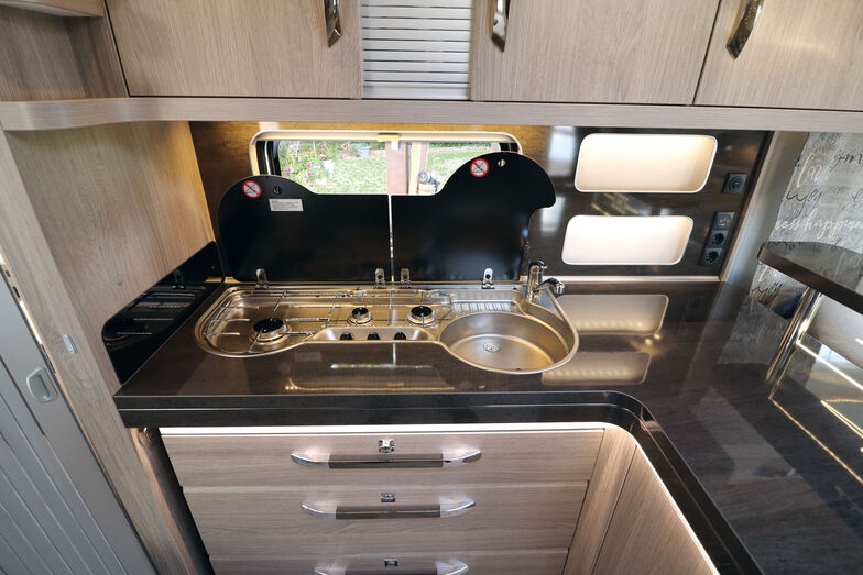 La cuisine d’angle avec plan de travail latéral offre de nombreux espaces de rangement, un grand plan de travail et une multitude de sources de lumière.