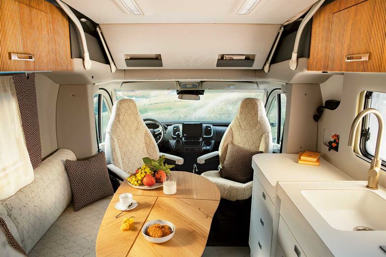 Wohnlich trotz Kompaktmass: der Wohnraum des Oasi 540.1 mit L-förmiger Sitzecke, drehbaren Cockpit-Sitzen, verschiebbarem Tisch und Küchenzeile.